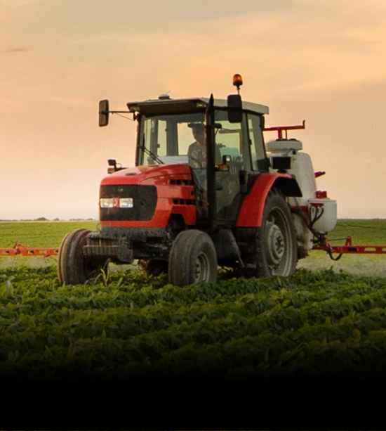 A red tractor in a green agricultural field during sunset, symbolizing modern farming technology for enhanced productivity.