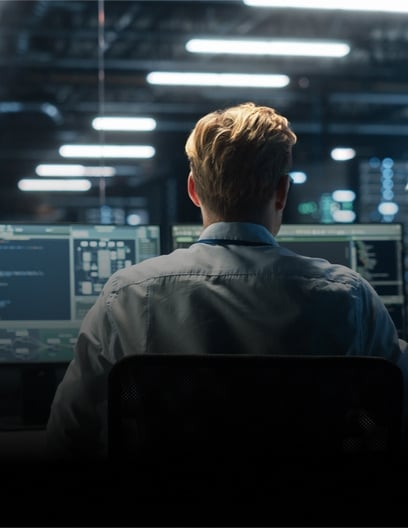 A rear view of a person working in a high-tech lab filled with multiple computer screens, representing 35 Centers of Excellence dedicated to innovation.