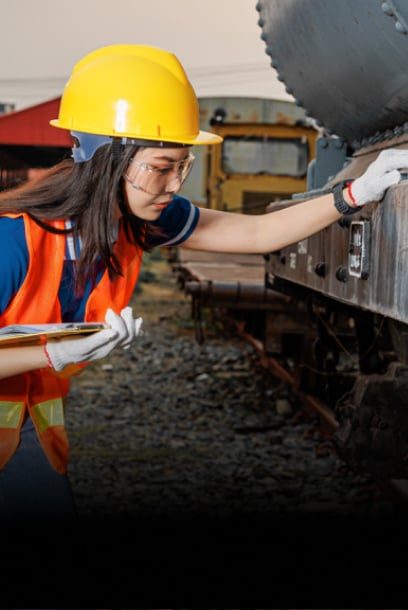 A technician in safety gear inspecting train components for aftermarket support and operations.
