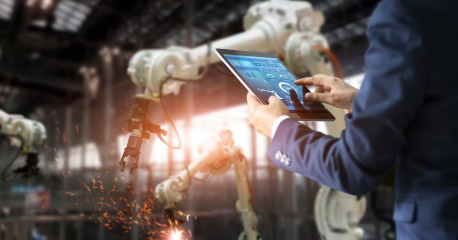  A professional using a tablet to monitor robotic arms in an industrial setting showcasing IoT-driven analytics.