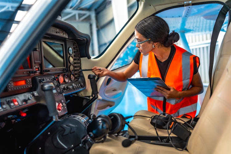 Female aircraft maintenance engineer using checklist while inspecting control panel inside cockpit of light aircraft